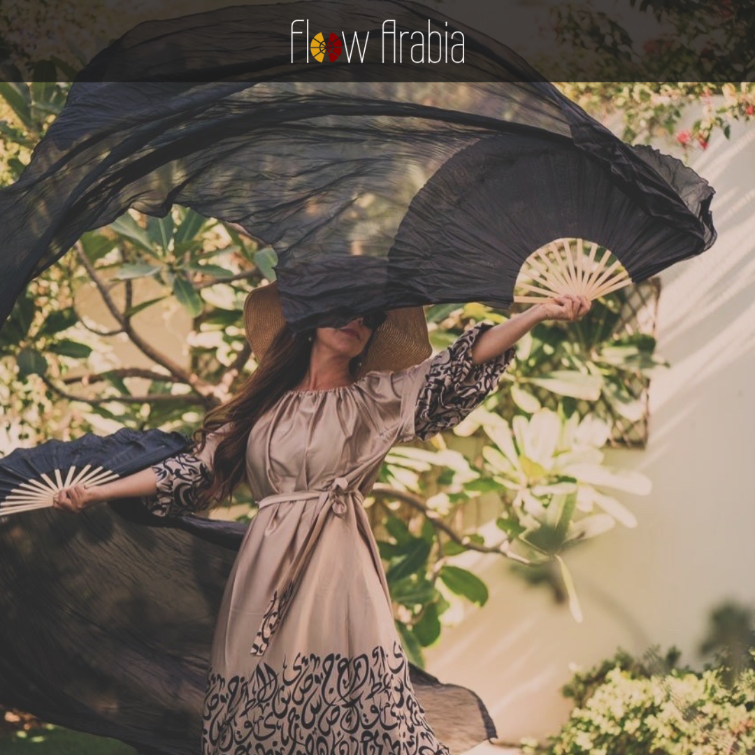 Woman in a long dress holding a large black fan with 'Flow Arabia' branding.